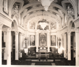 Intérieur de la belle église avec jardinières décoratives suspendues de la voûte. Vous remarquez que l'autel est placé au pied de la peinture centrale de la scène de la crucifixion du Christ.
Decorative flower pots suspended from the cathedral ceiling. The altar is placed below the central painting of the crucifixion of Christ.
